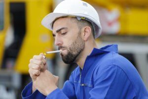 Man in white hardhat lighting a cigarette