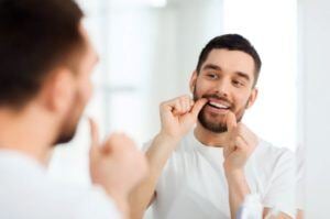 Young man flossing teeth in front of mirror