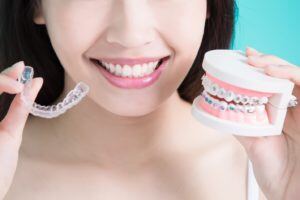 Young woman holding invisalign braces and set of false teeth